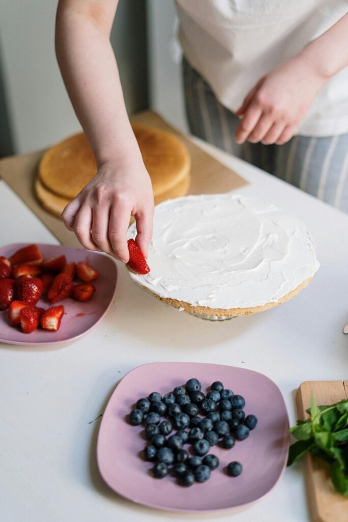 in this image cake designer making custom cakes with strawberries and blueberries.